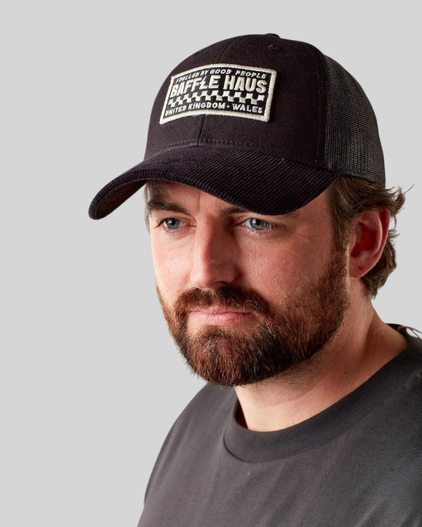 Man wearing a black Baffle Haus trucker cap with a structured front panel and breathable mesh back