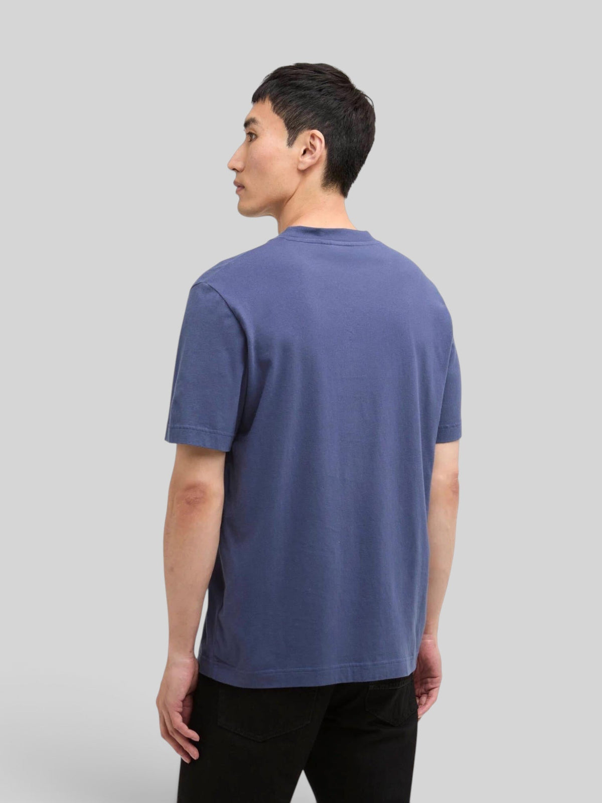 A man wearing a plain blue Baffle Haus International Shifter cotton t-shirt, back view against a grey background.