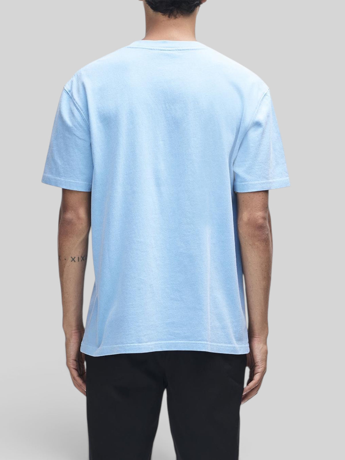 Back view of a model wearing a Baffle Haus Shield garment dyed box fit t-shirt in bonnie blue recycled cotton.