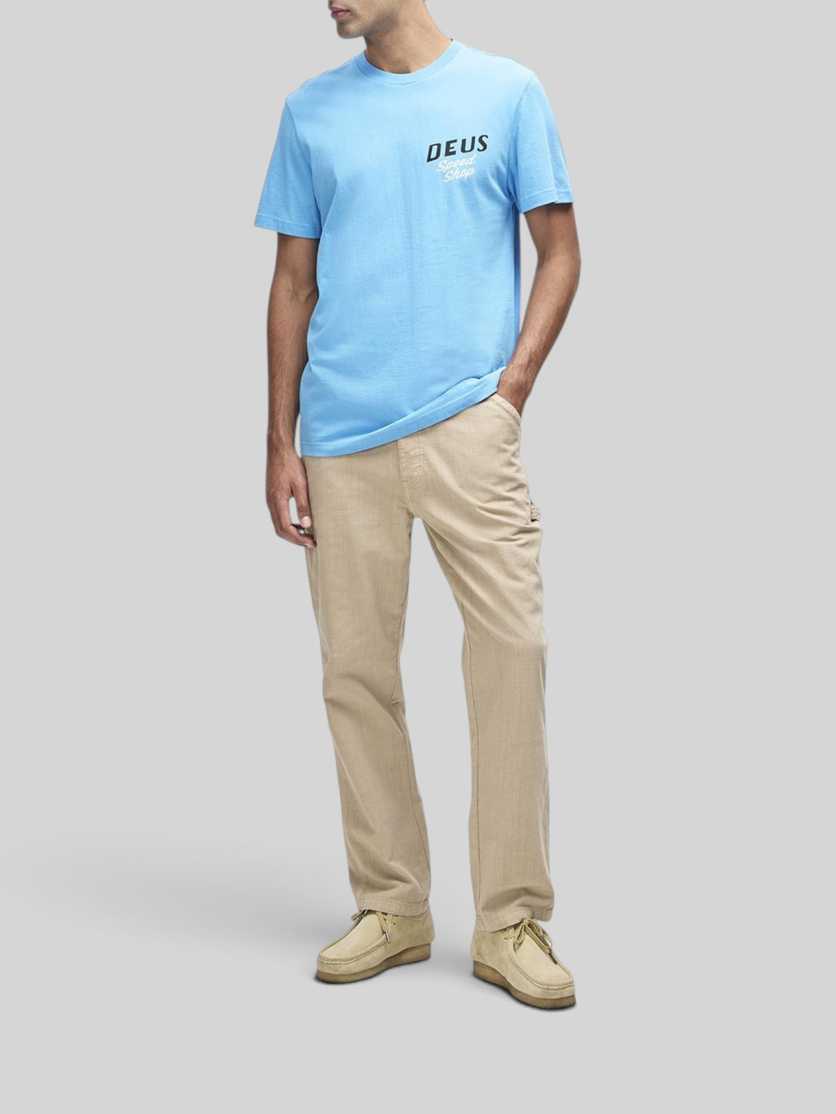 Baffle Haus Dogleg Tee in Bonnie Blue with chest graphic, worn by a model with beige trousers and suede shoes.