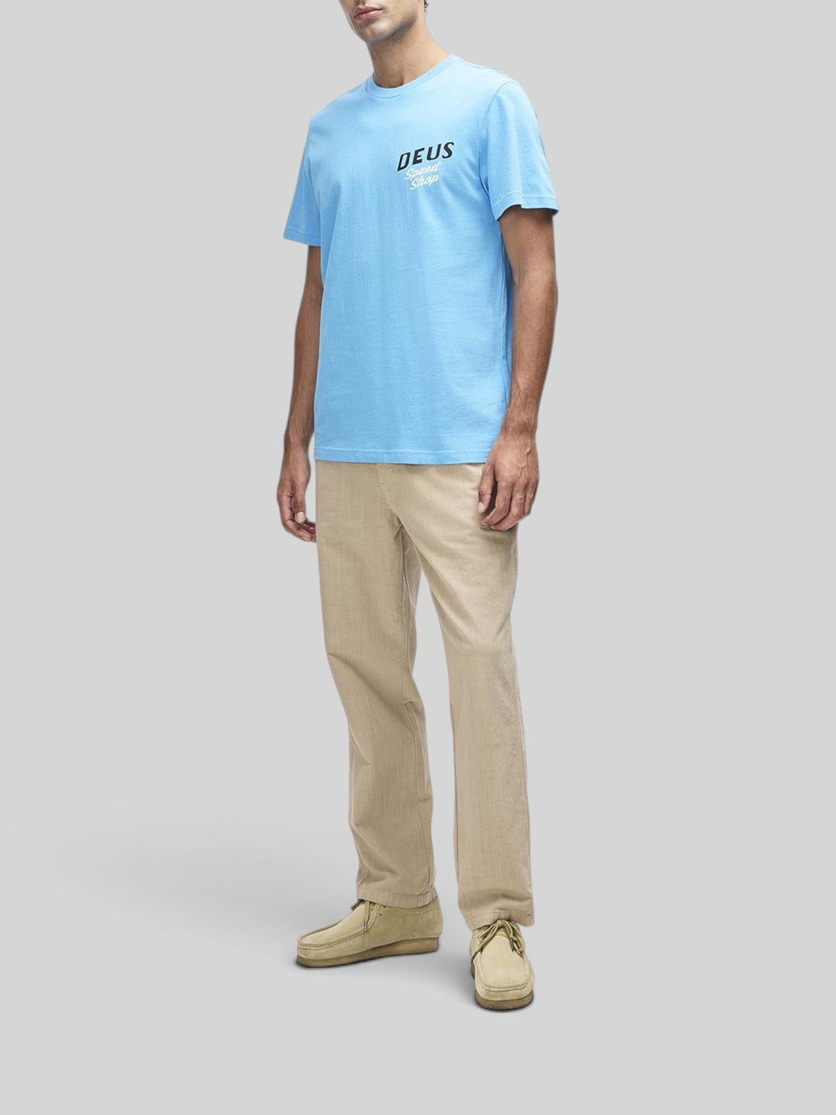 Baffle Haus Dogleg Tee in bonnie blue featuring a chest graphic, worn with beige trousers and suede shoes.