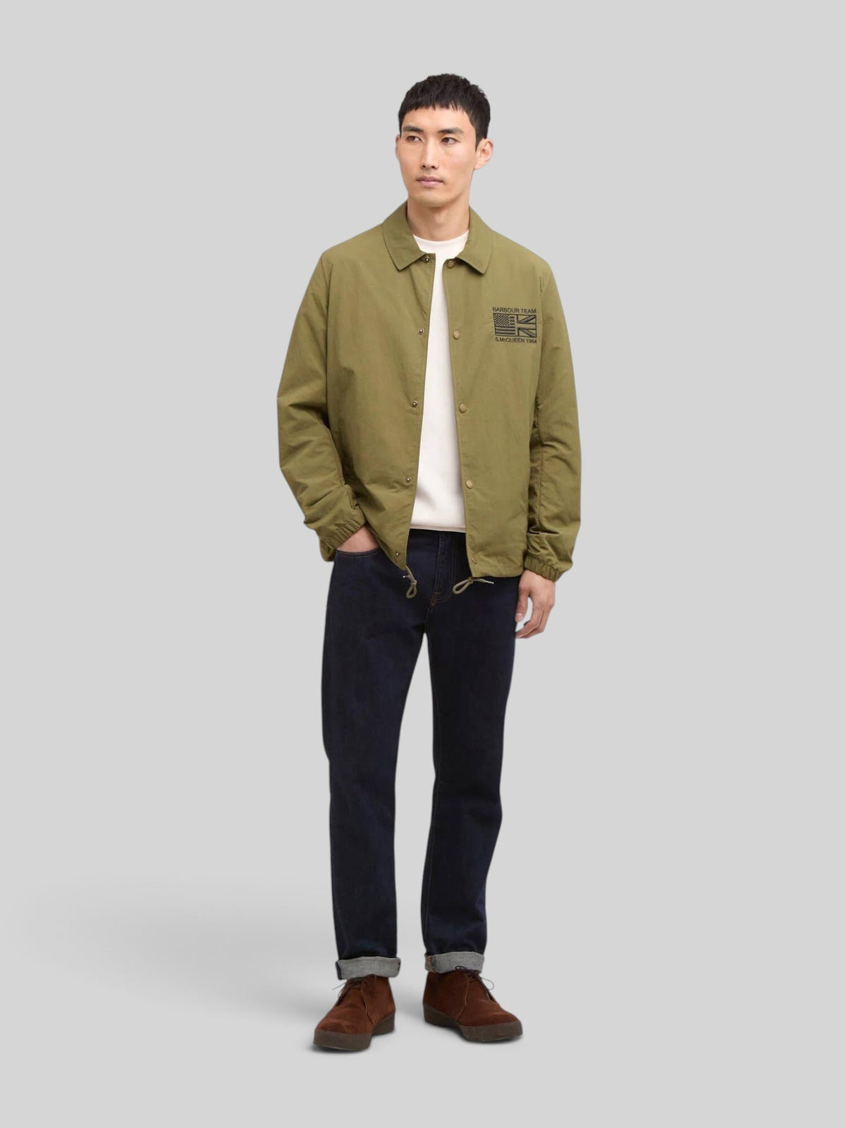 Baffle Haus International Coach Casual Jacket in burnt olive with stud fastening, collar, and Steve McQueen embroidery.