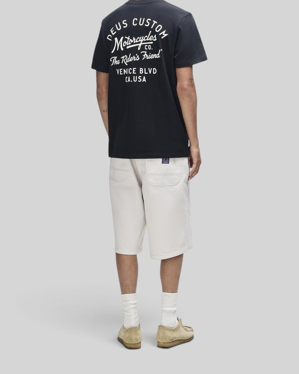 Baffle Haus Camber Tee in black with white back graphic, paired with beige shorts and suede shoes, rear view