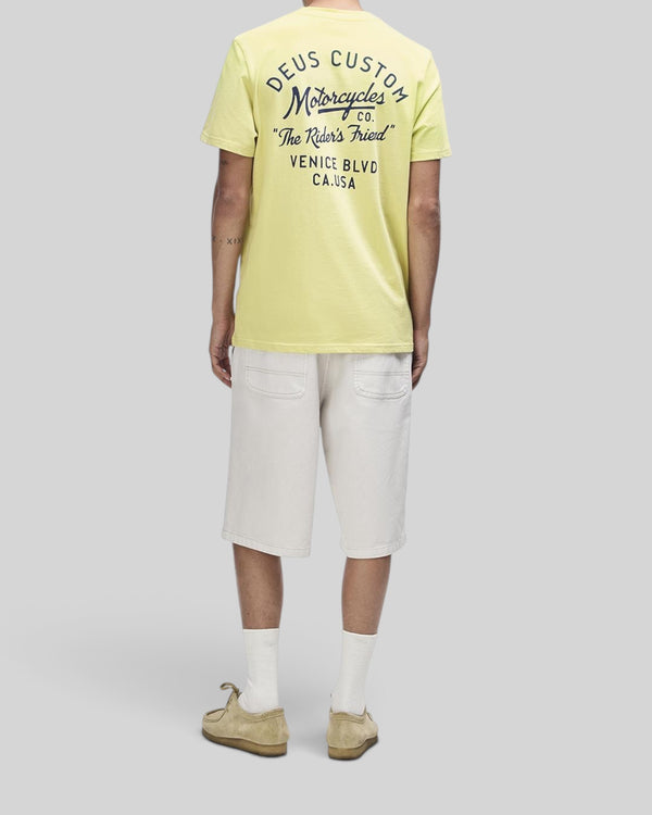 Baffle Haus Camber Tee in canary yellow with back graphic print, worn with beige shorts and casual shoes