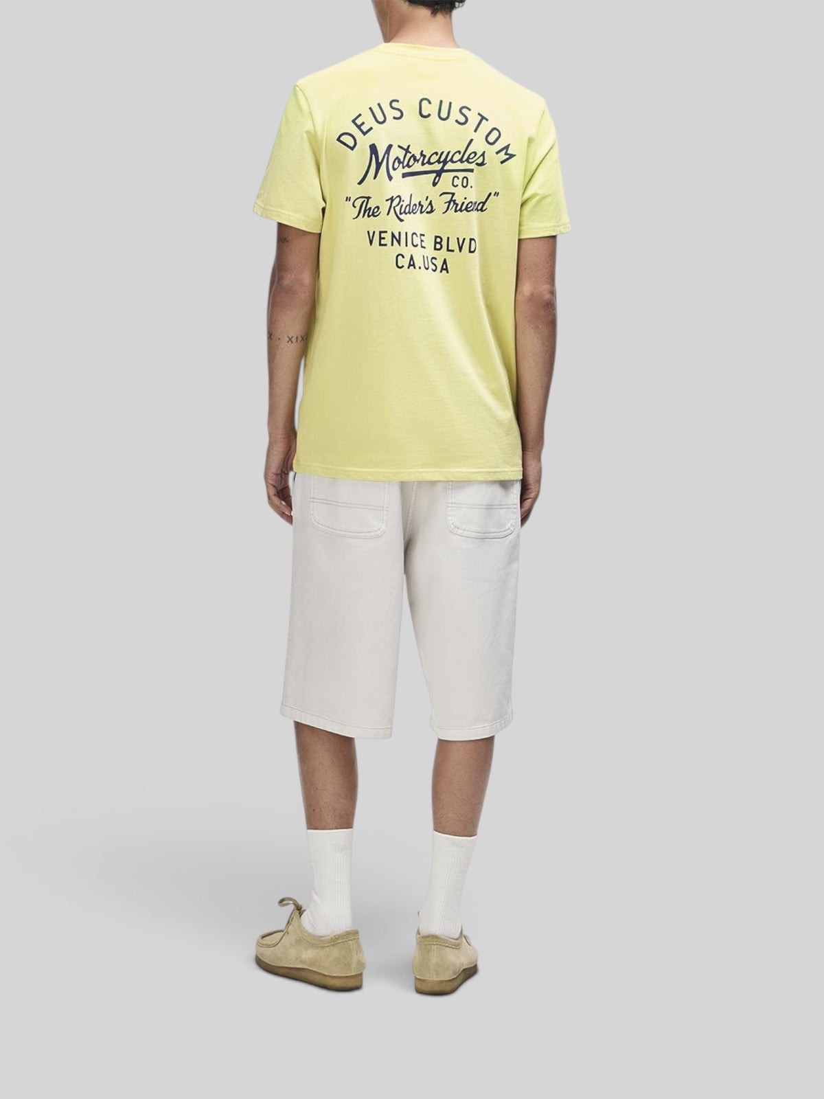 Baffle Haus Camber Tee in canary yellow with back graphic print, worn with beige shorts and casual shoes