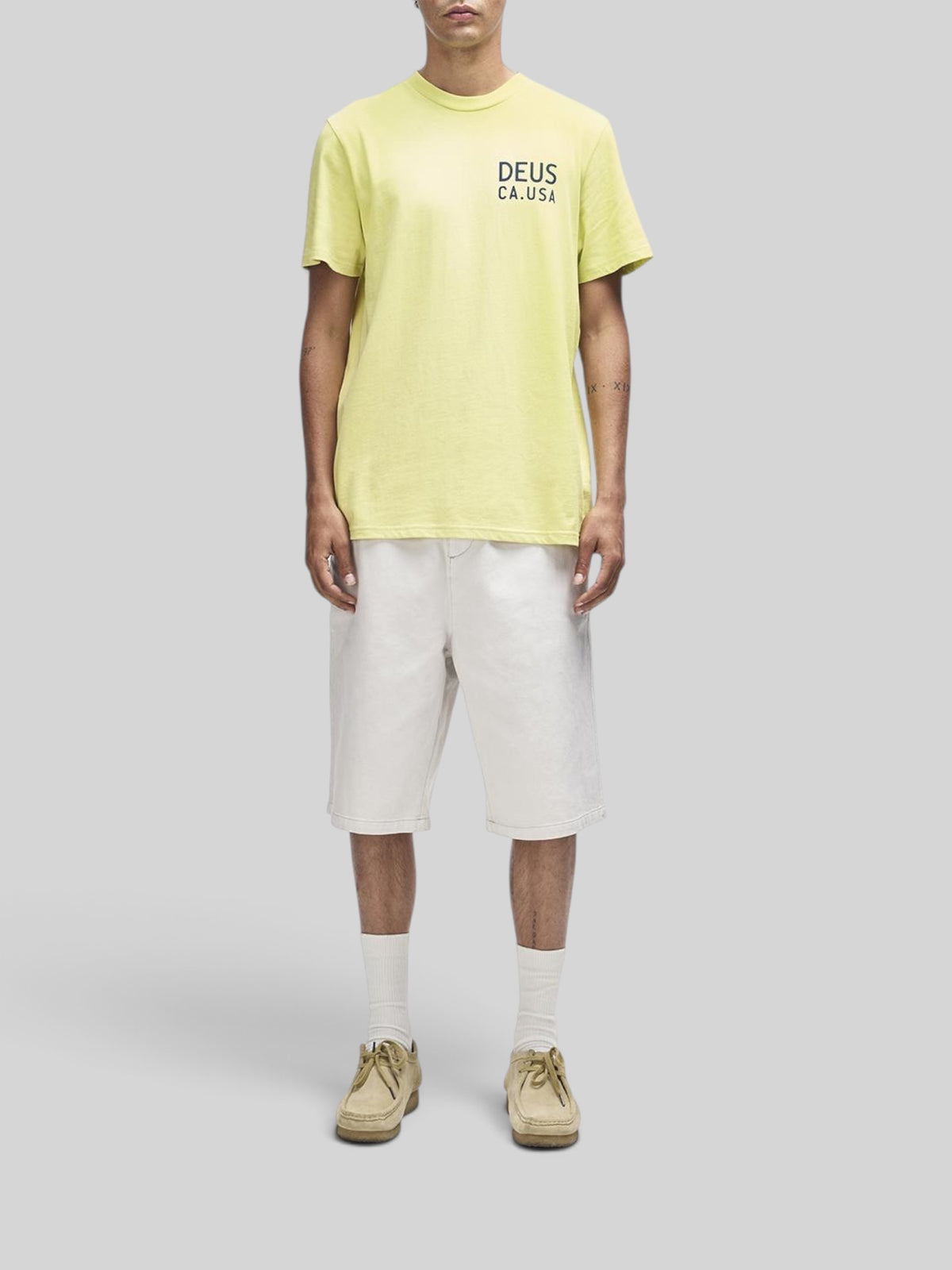 Baffle Haus Camber Tee in canary yellow with chest print, worn with white shorts and tan shoes on a model.