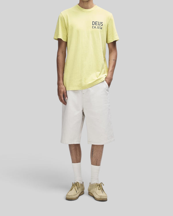 Baffle Haus Camber Tee in canary yellow, regular fit short sleeve shirt with chest print, worn with white shorts.