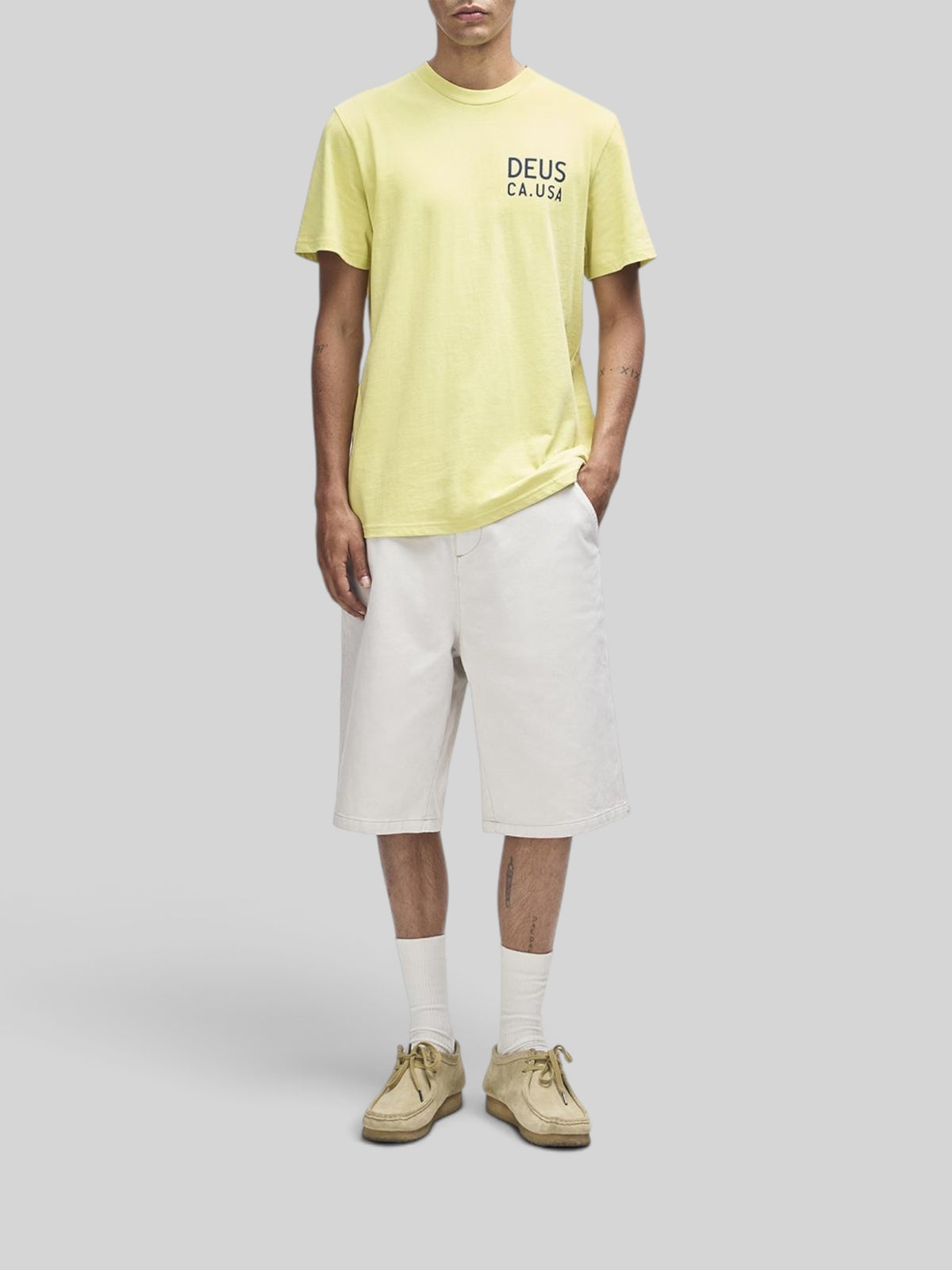 Baffle Haus Camber Tee in canary yellow, regular fit short sleeve shirt with chest print, worn with white shorts.