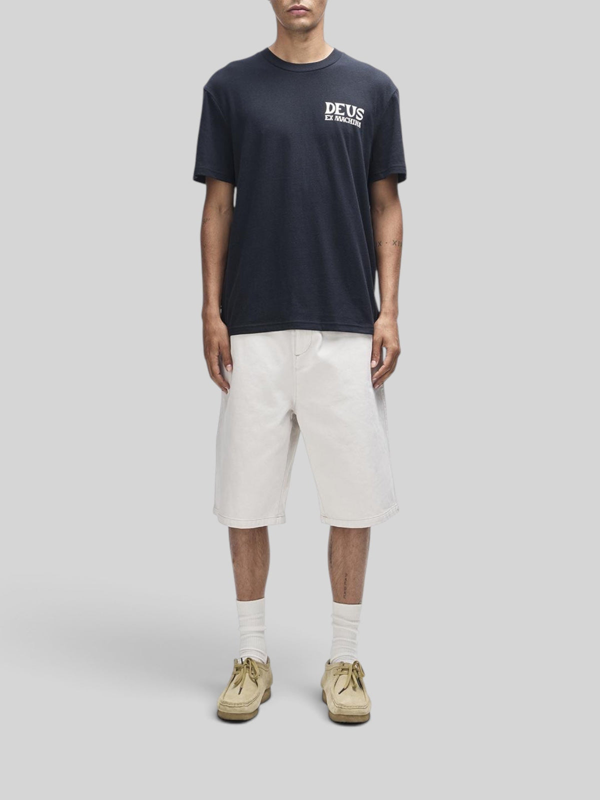 Baffle Haus Chinook black box fit t-shirt with chest print, worn with off-white shorts and tan suede shoes.