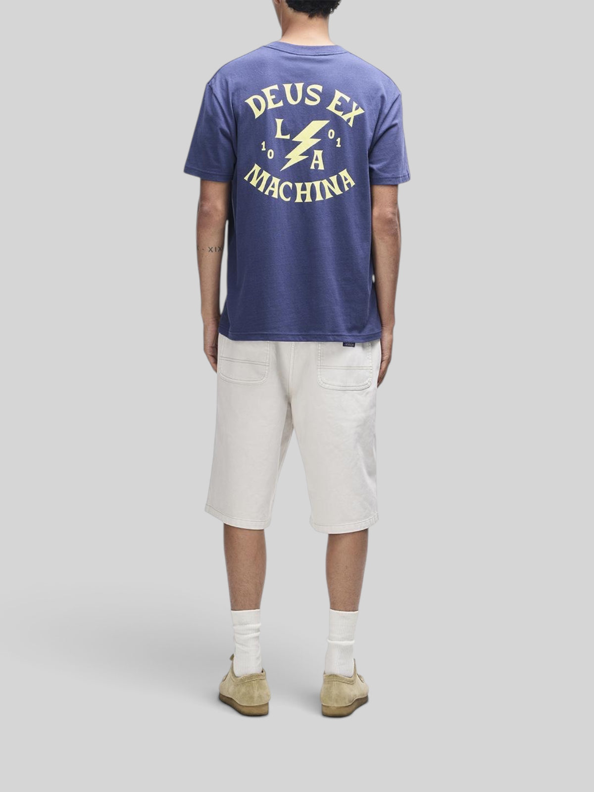 Baffle Haus Chinook Tee in mechanic blue with back graphic print, worn with off-white shorts and suede shoes