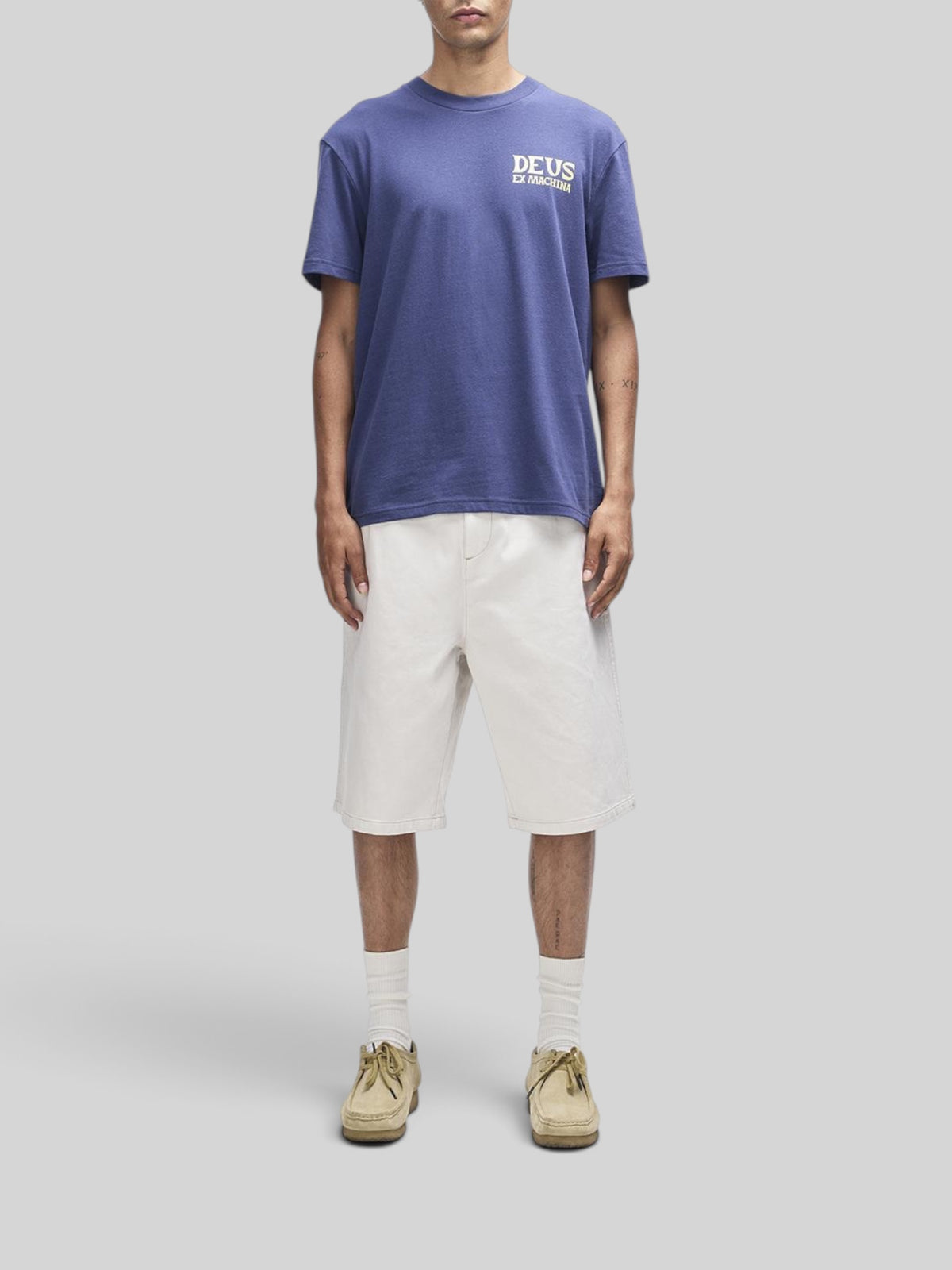 Baffle Haus Chinook Tee in mechanic blue with chest logo, worn by a model with white shorts and beige shoes.