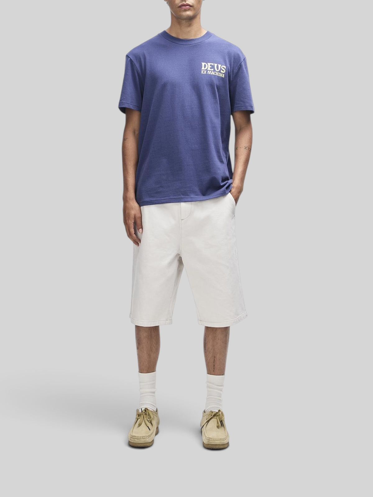 Baffle Haus Chinook Tee in mechanic blue with chest logo, worn by a model with white shorts and beige shoes.