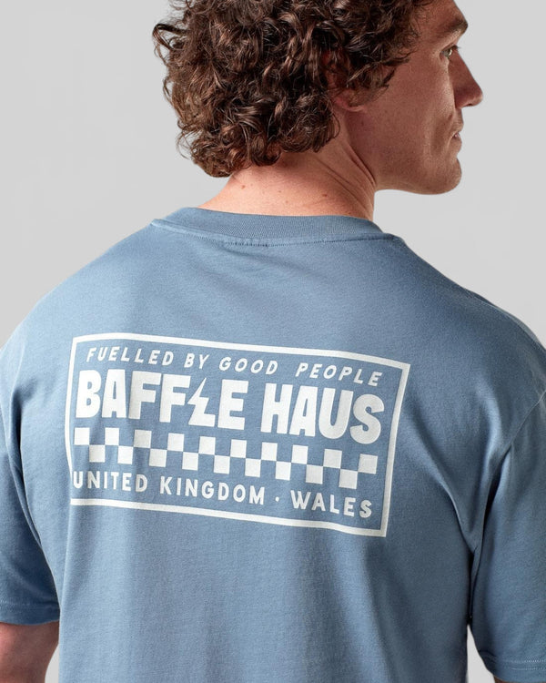 Baffle Haus Flags Tee in coastal blue cotton with a white graphic print on the back, worn by a male model.