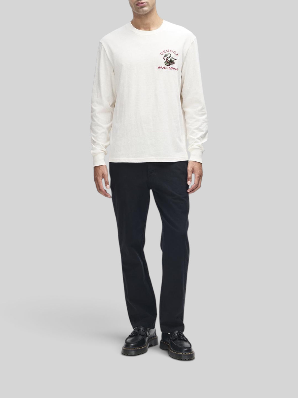 Baffle Haus Danger Noodle long sleeve tee in dirty white with chest embroidery, worn by a model with black trousers.