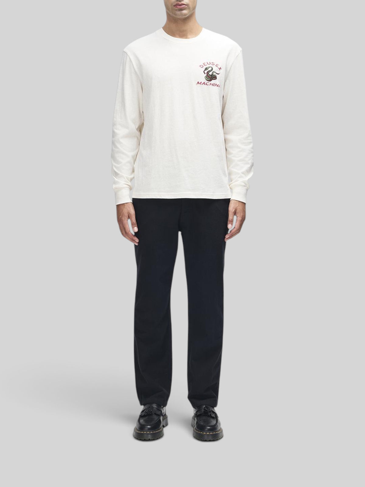 Baffle Haus Danger Noodle long sleeve tee in dirty white with chest embroidery, worn by a model with black trousers.