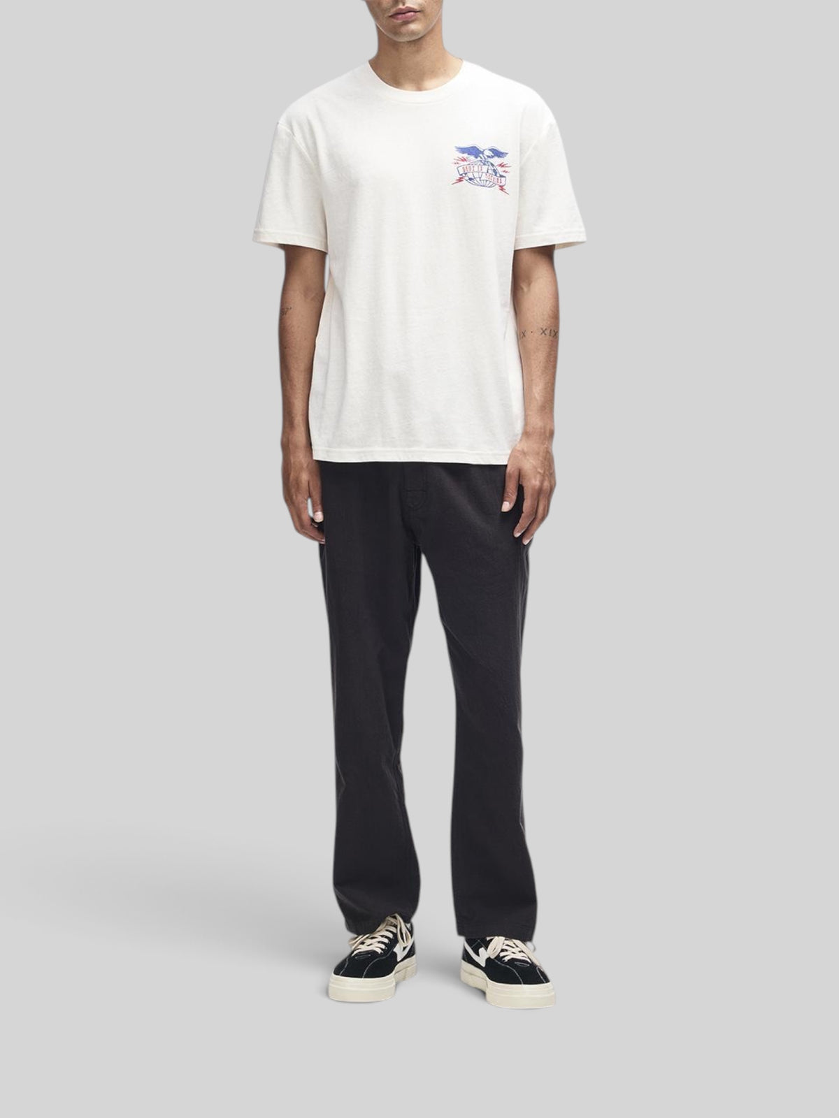 Baffle Haus Claw-Some Whizz Tee in dirty white with chest graphic, worn by a model with black trousers and sneakers.