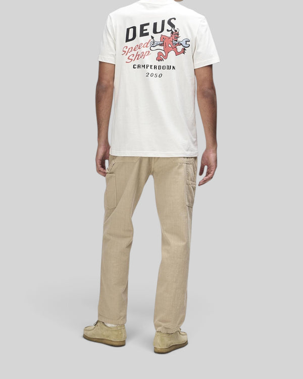 Baffle Haus Dogleg Tee in dirty white featuring back graphic print, worn with beige cargo pants and suede shoes.