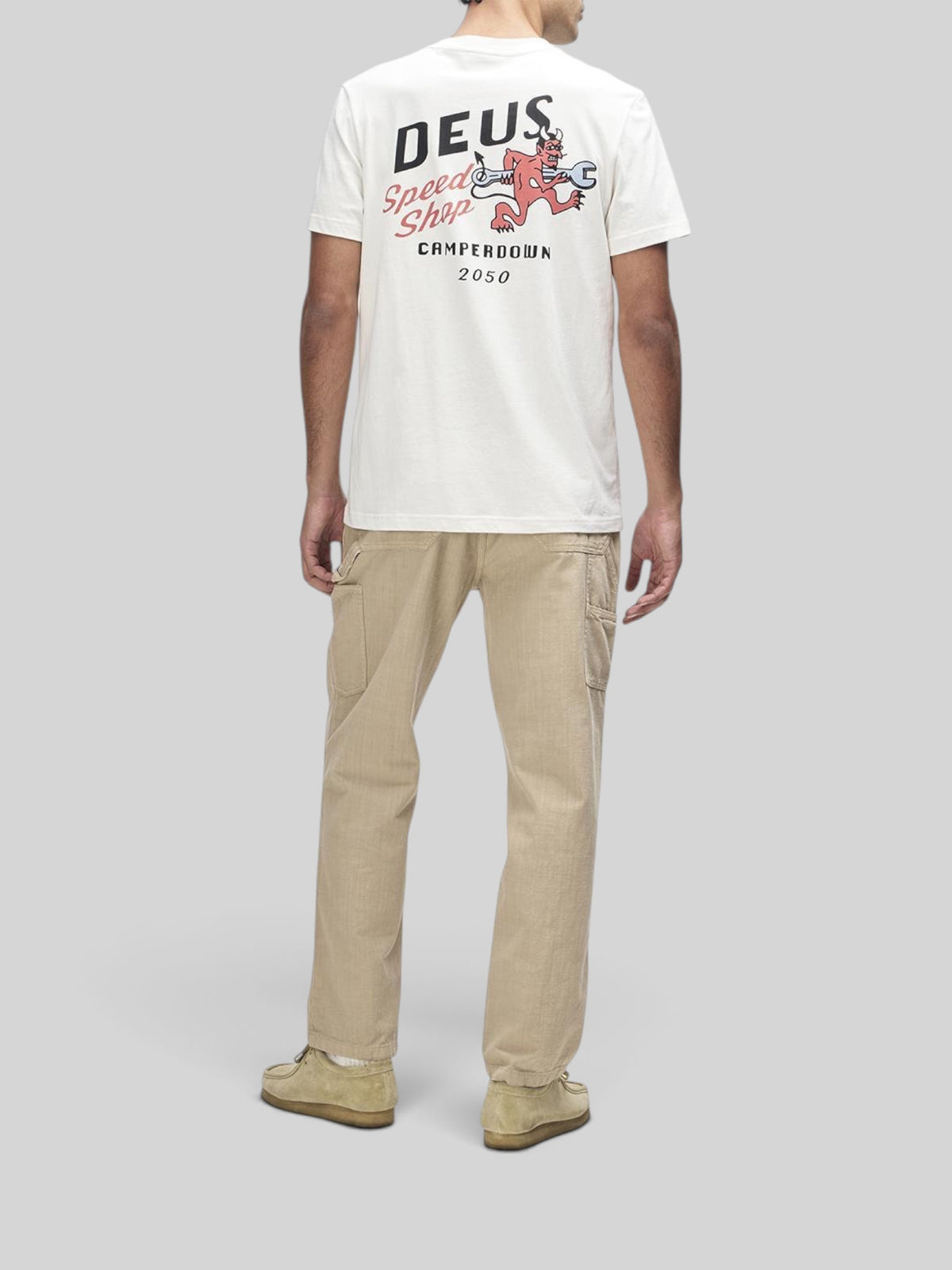 Baffle Haus Dogleg Tee in dirty white featuring back graphic print, worn with beige cargo pants and suede shoes.
