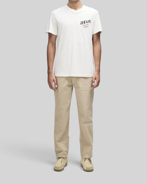 Baffle Haus Dogleg Tee in dirty white with chest graphic, worn by a model with beige trousers and suede shoes.