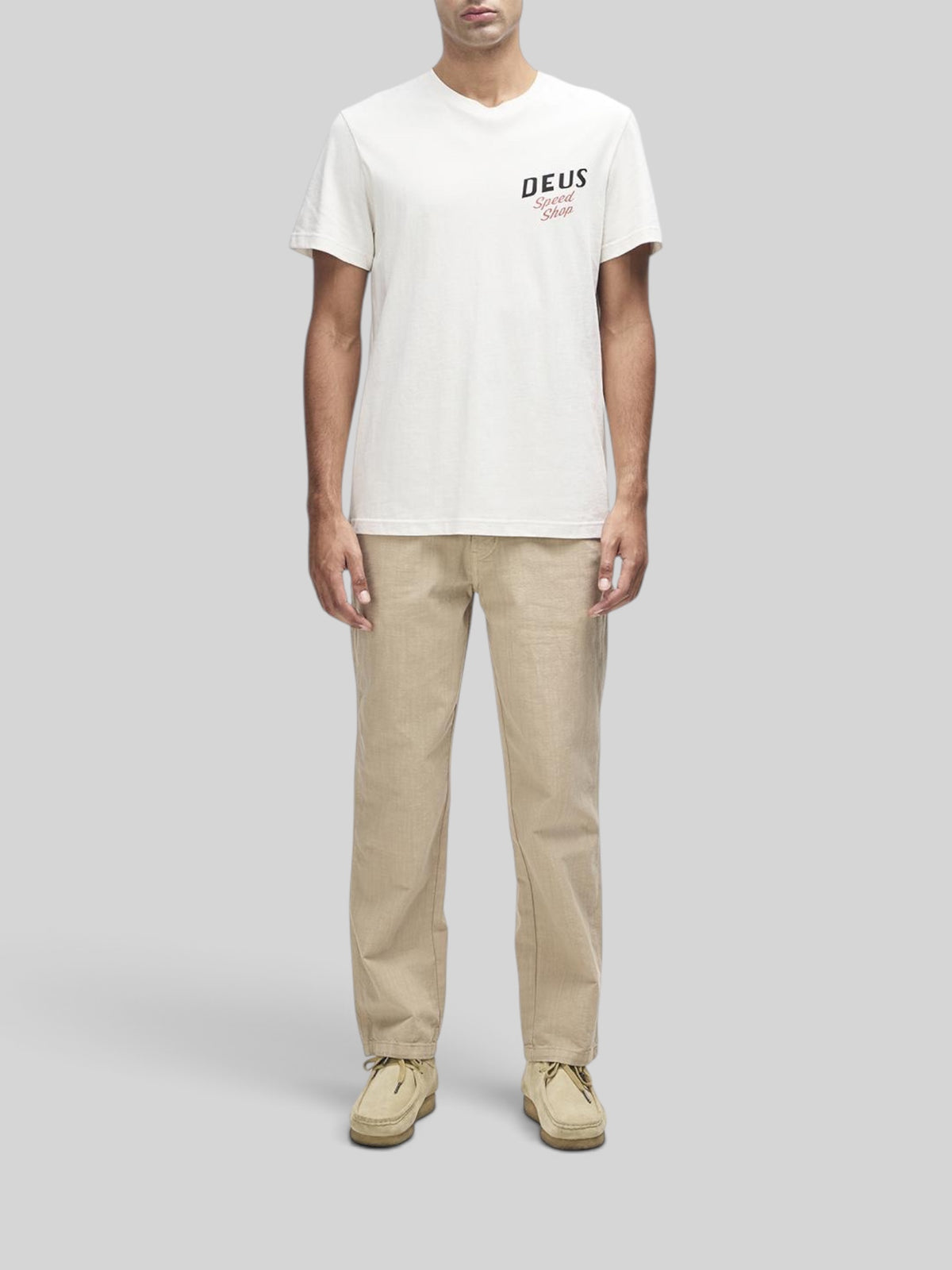 Baffle Haus Dogleg Tee in dirty white with chest graphic, worn by a model with beige trousers and suede shoes.