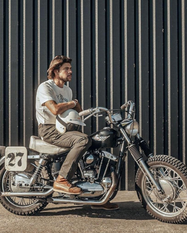 Baffle Haus El Mirage off-white cotton t-shirt with vintage winged wheel graphic worn by a man on a classic motorcycle