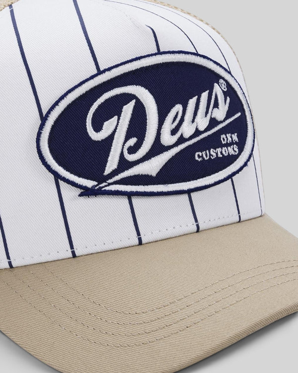Baffle Haus Forecourt Trucker cap in white with navy pinstripes, tan brim, and Deus Customs oval patch.