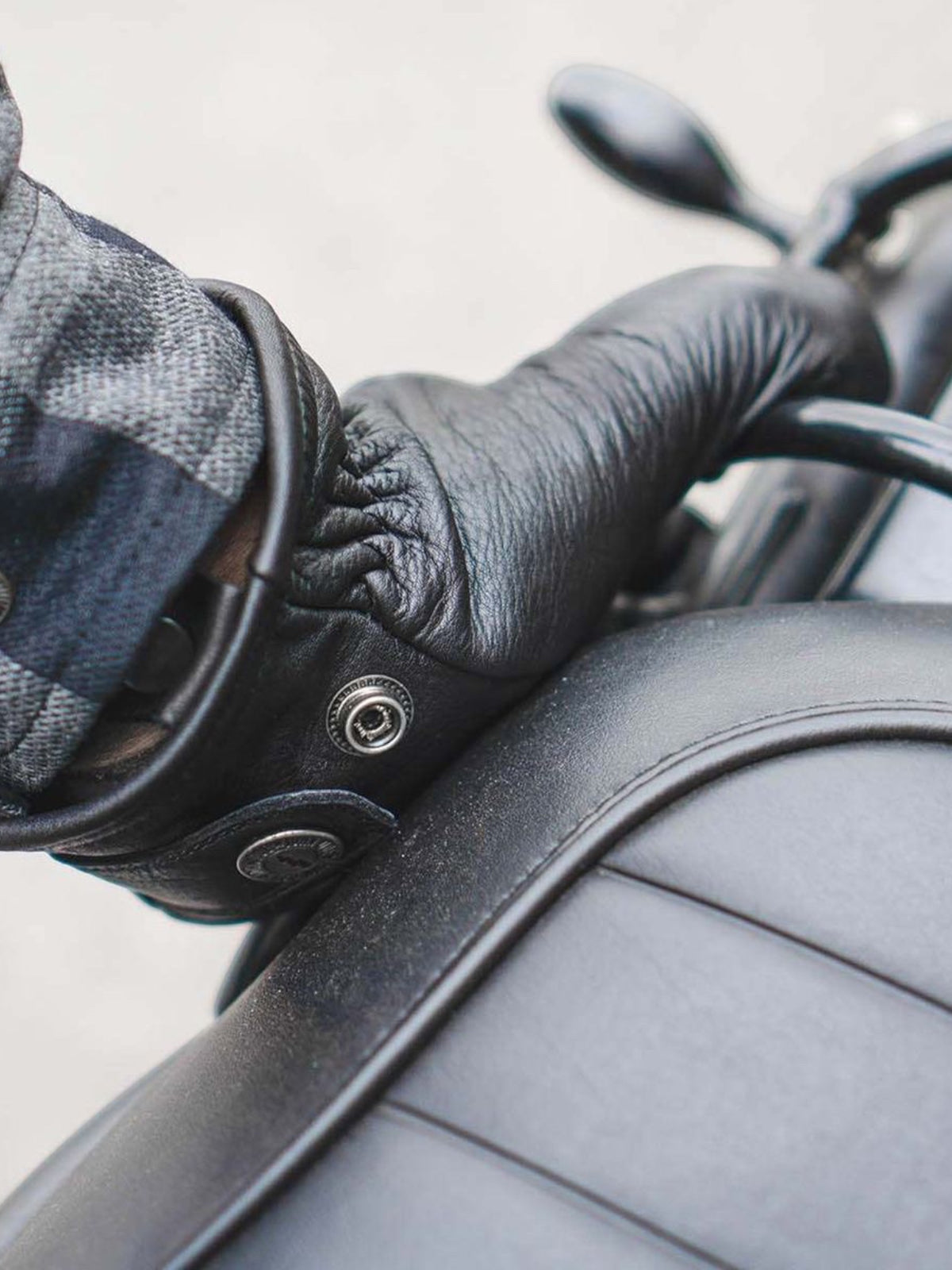 Baffle Haus Freewheeler XTM black cowhide leather motorcycle gloves with press-stud wrist closure on a bike seat