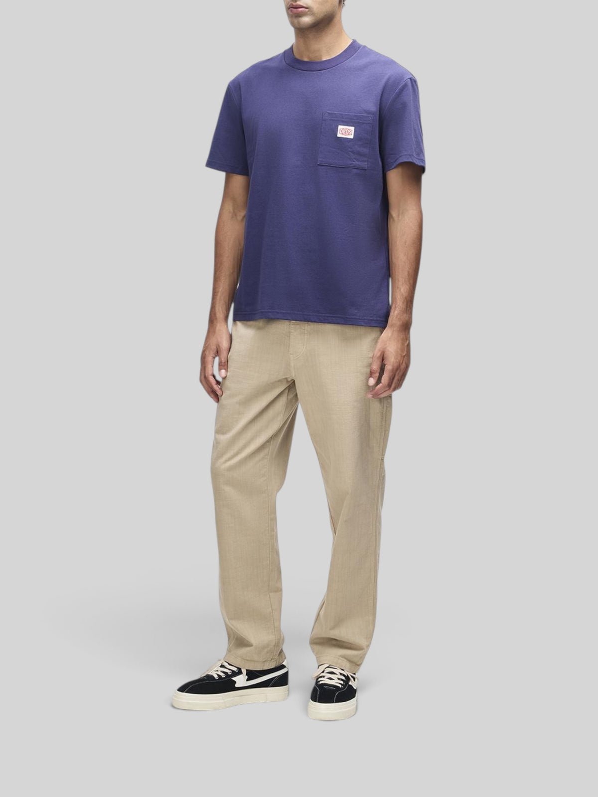 Baffle Haus French Blue box fit short sleeve t-shirt with a chest pocket and brand label, worn with beige trousers.