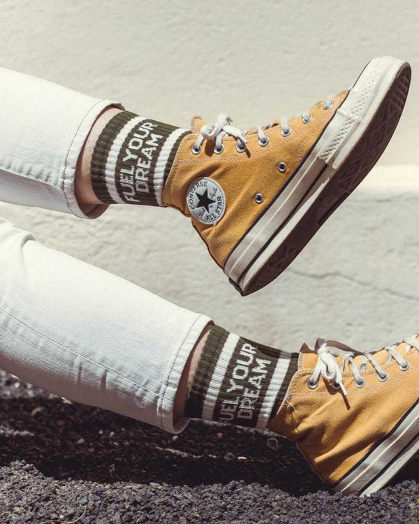 Baffle Haus Fuel Your Dreams olive green socks with white stripes and text worn with mustard yellow high-top sneakers