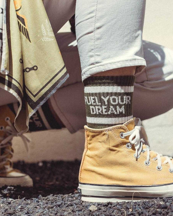 Baffle Haus Fuel Your Dreams socks in olive green with white stripes and text worn with yellow high-top sneakers