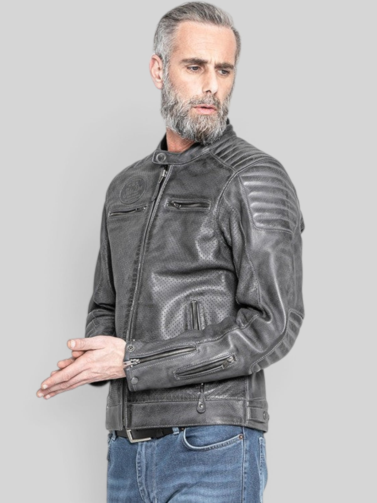 Baffle Haus grey perforated leather motorcycle jacket with padded shoulders and zippered cuffs worn by a bearded man