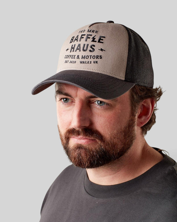 Man wearing a grey Baffle Haus Coffee & Motors trucker cap with a structured front panel and breathable mesh back