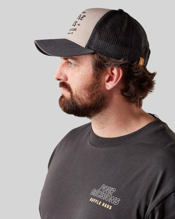 Baffle Haus Coffee & Motors grey and black trucker cap with mesh back worn by a man in profile view