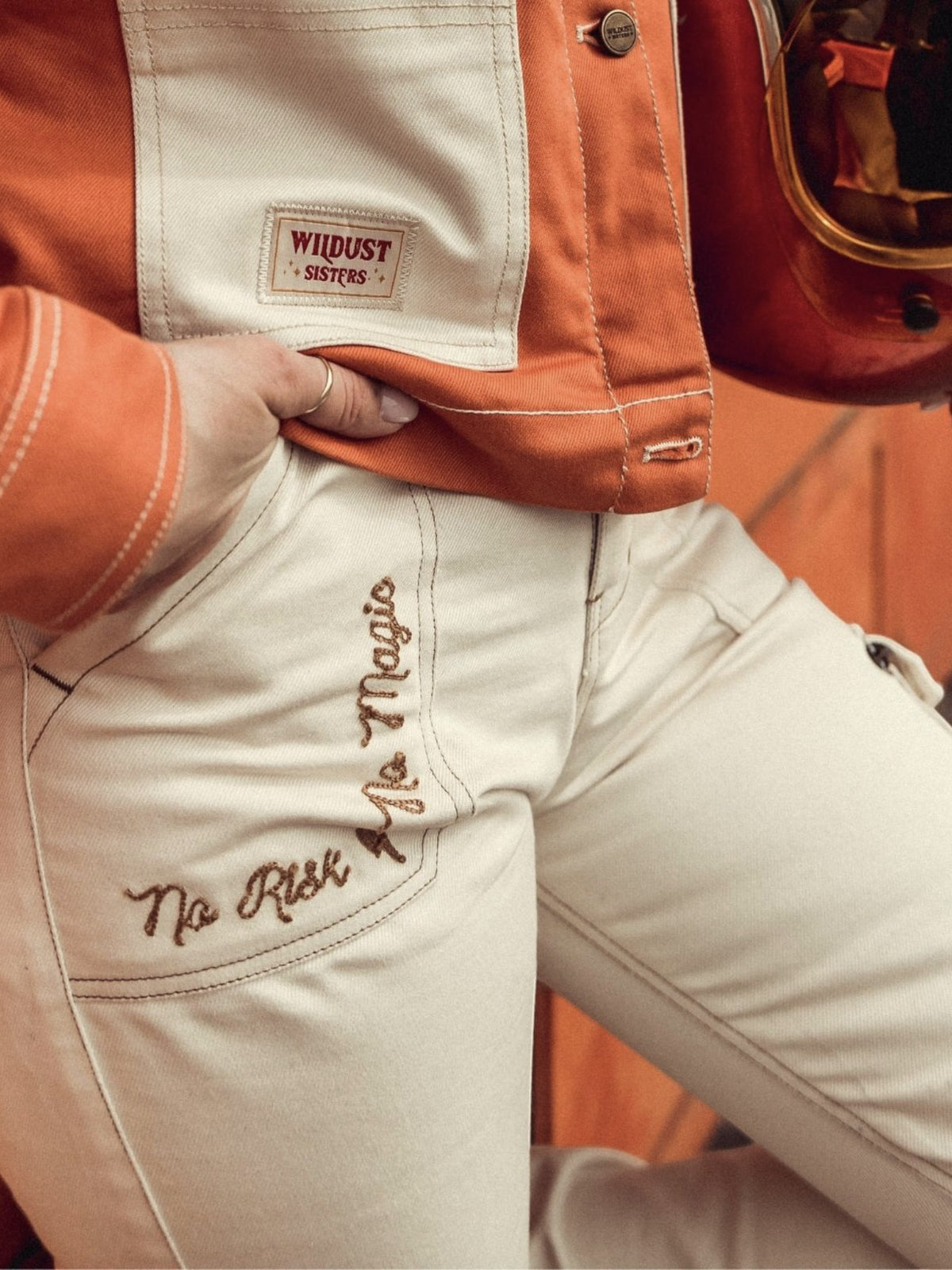 Baffle Haus ivory cargo motorcycle trousers with embroidered detail and contrasting stitching worn with orange jacket