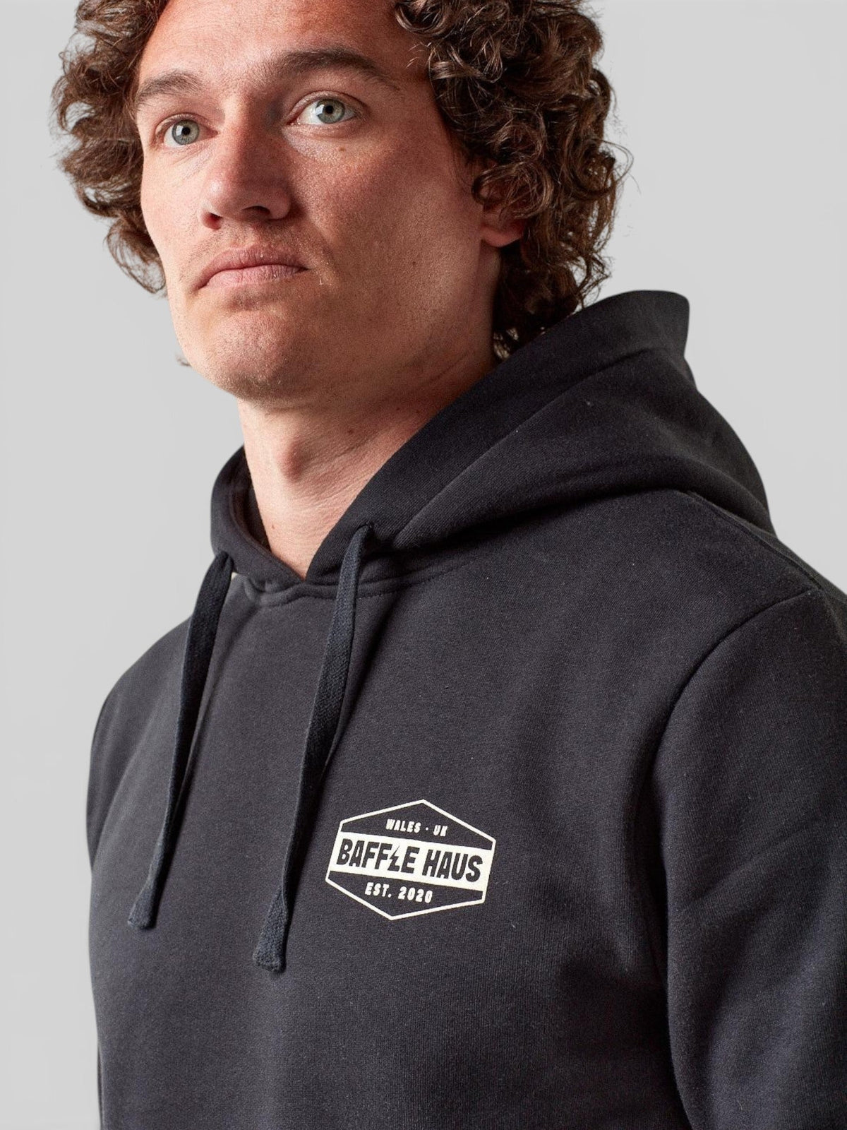 Baffle Haus jet black heavyweight cotton blend hoodie with white chest logo, worn by a man with curly brown hair.