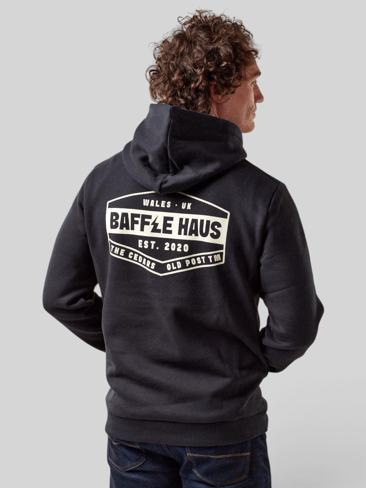Baffle Haus jet black retro hoodie with white graphic logo on the back, worn by a man against a grey background