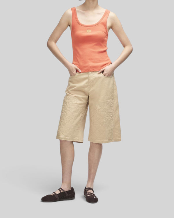 Baffle Haus June Shield Tank in flame orange with thin straps and chest embroidery, worn with beige quilted shorts.