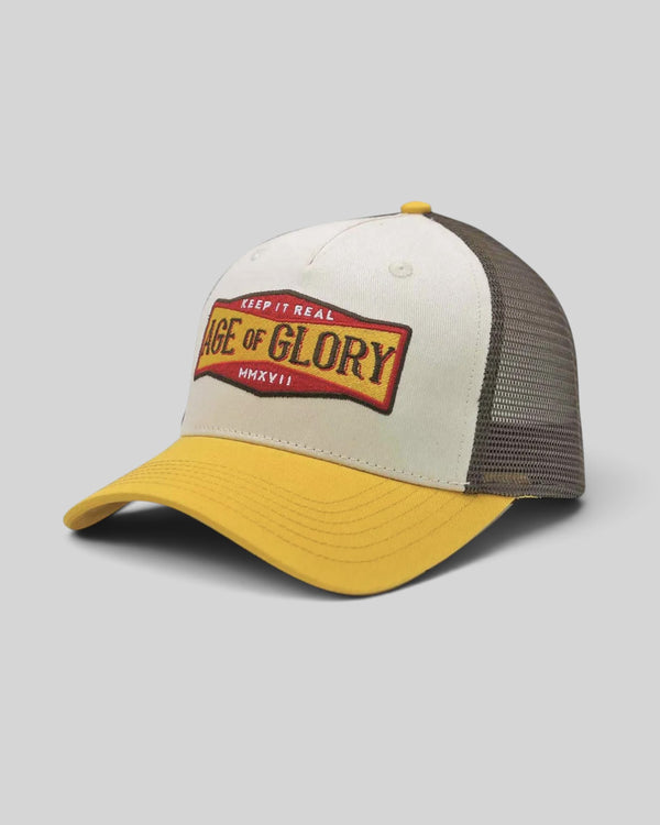Baffle Haus Keep It Real trucker cap in white and yellow with a vintage graphic patch and brown mesh back panel.