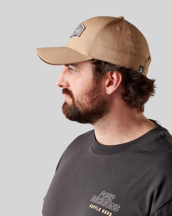 Man wearing a khaki Baffle Haus baseball cap with a structured crown and curved brim in a side profile view.