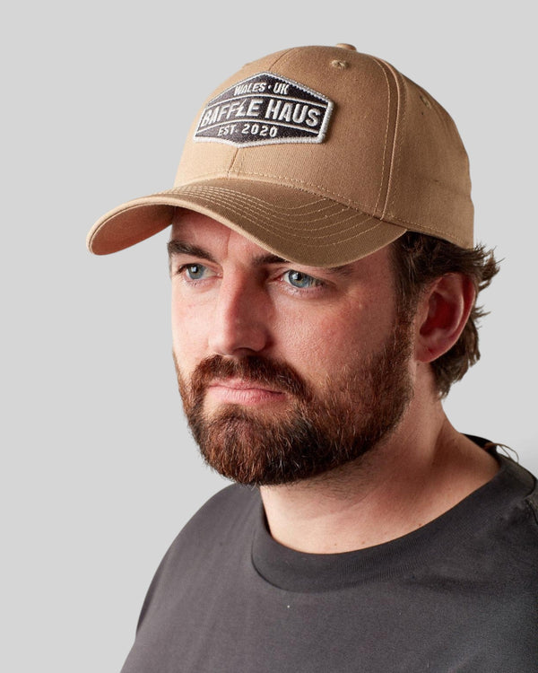 A man wearing a khaki Baffle Haus baseball cap with a structured crown, curved brim, and branded patch detail.