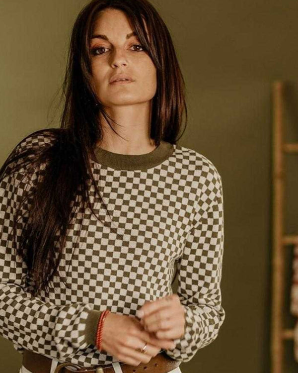 Baffle Haus khaki and white checkerboard knitted jumper with ribbed collar and cuffs worn by a woman