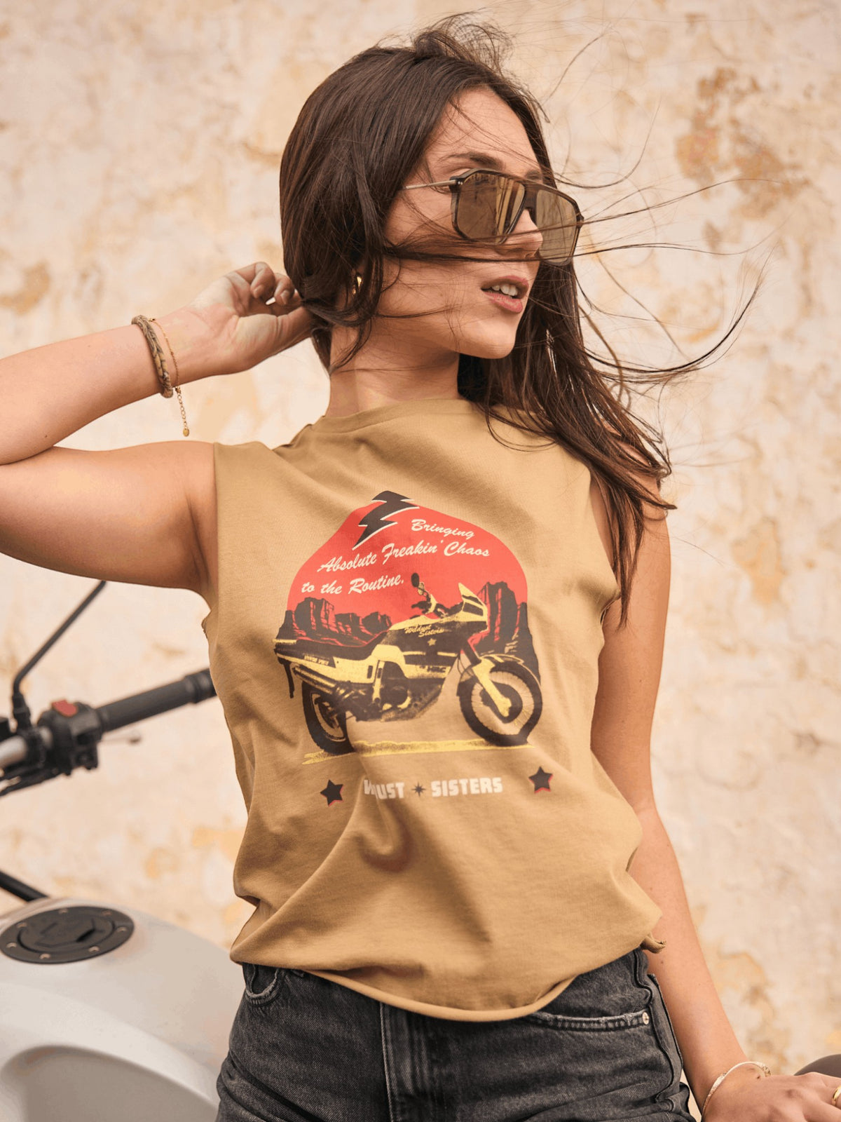 Baffle Haus khaki cotton tank top featuring a motorcycle graphic, worn by a woman with sunglasses near a motorbike.