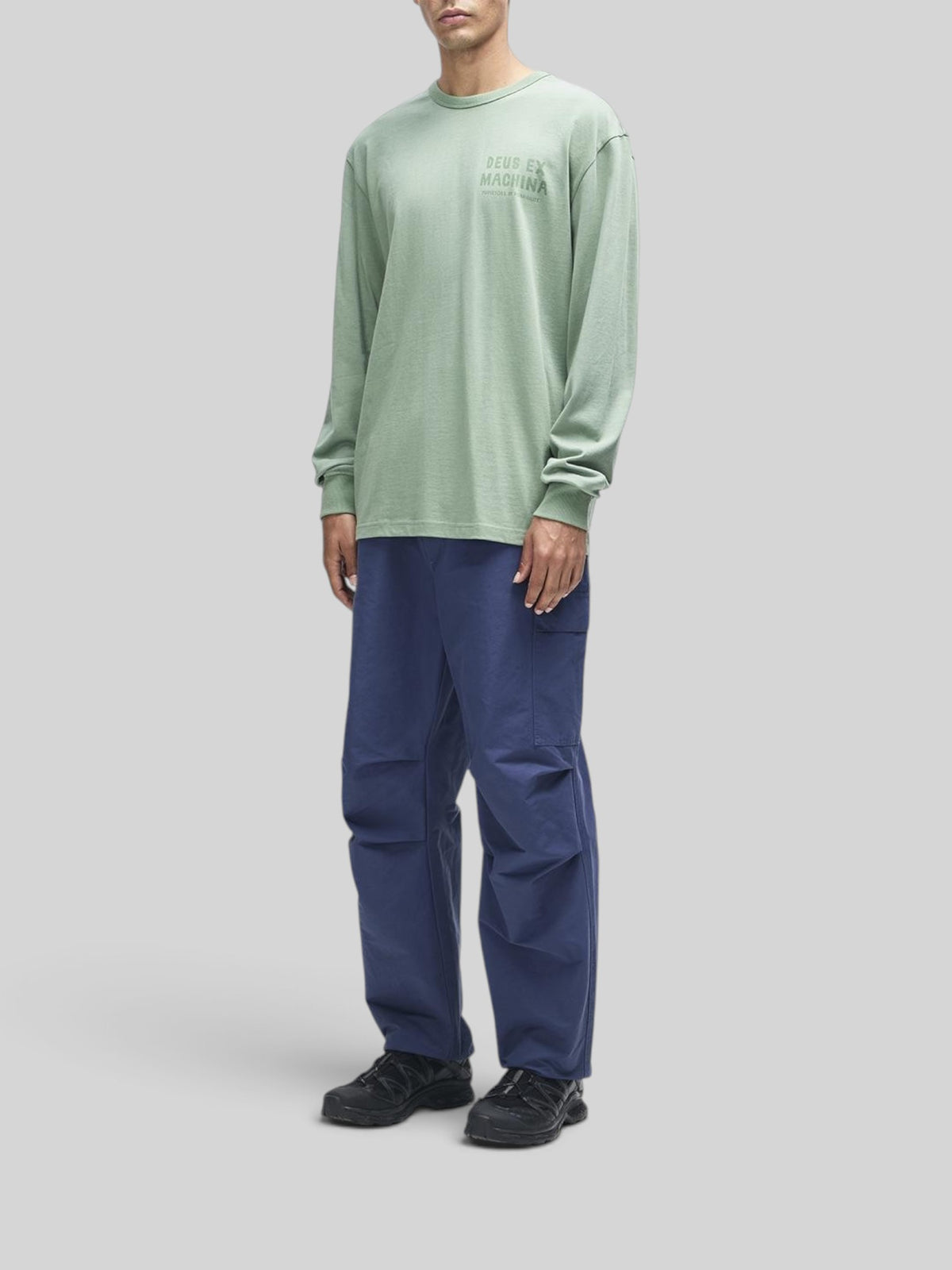 Baffle Haus Kumbaya long sleeve tee in loden frost green with chest graphic, worn by a model with blue cargo pants.