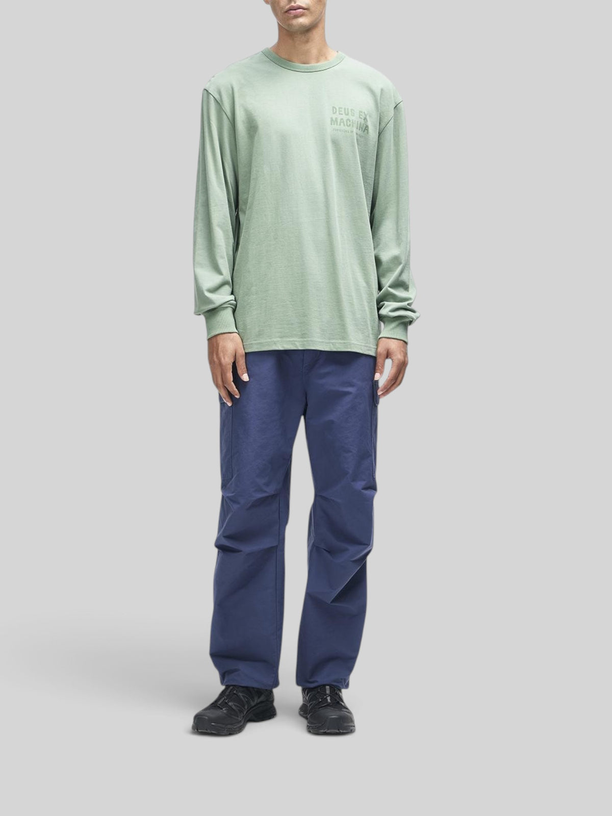 Baffle Haus Kumbaya long sleeve tee in loden frost green with chest graphic, worn by a model with blue trousers.