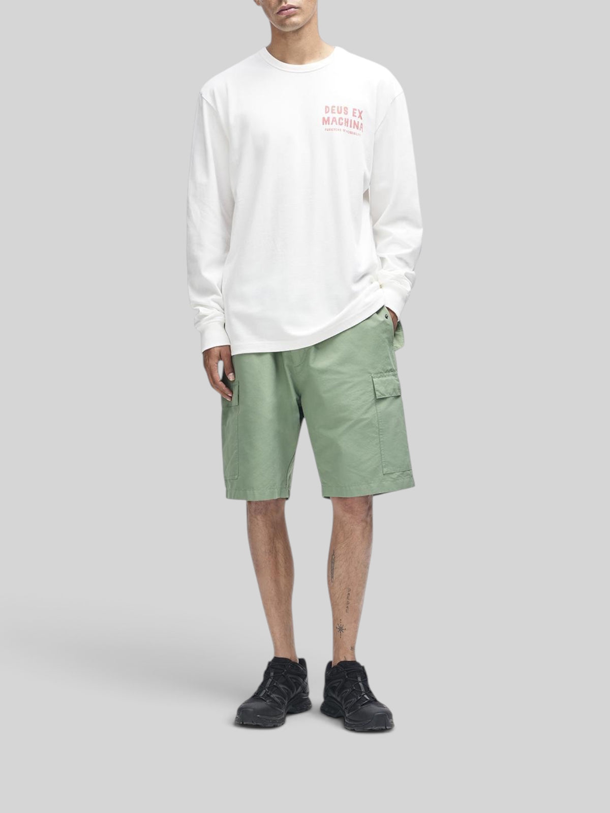 Baffle Haus Kumbaya long sleeve tee in vintage white with chest graphic, paired with green cargo shorts.