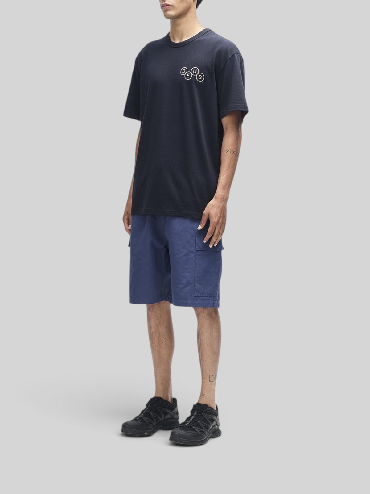 Baffle Haus Mechanism black short sleeve tee in organic cotton with chest graphic, worn with blue cargo shorts.