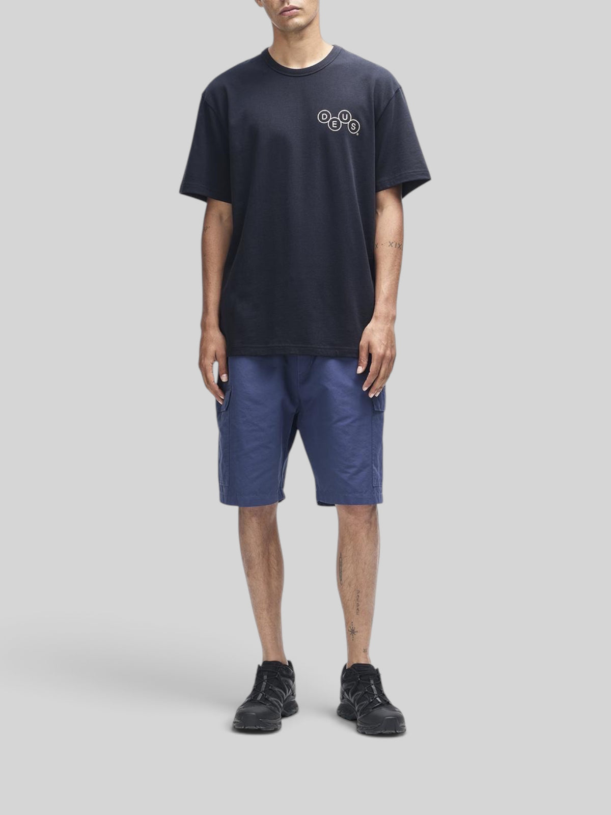 Baffle Haus Mechanism black short sleeve tee in organic cotton with chest graphic, worn with blue cargo shorts.
