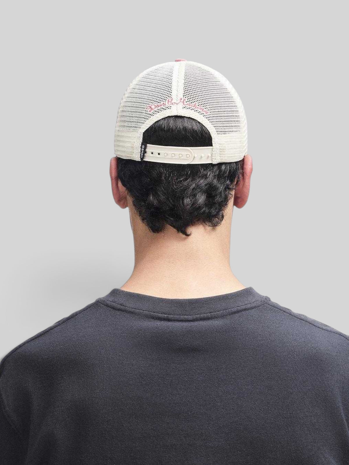 Rear view of a Baffle Haus melon red trucker hat with a white mesh back and adjustable plastic snap closure