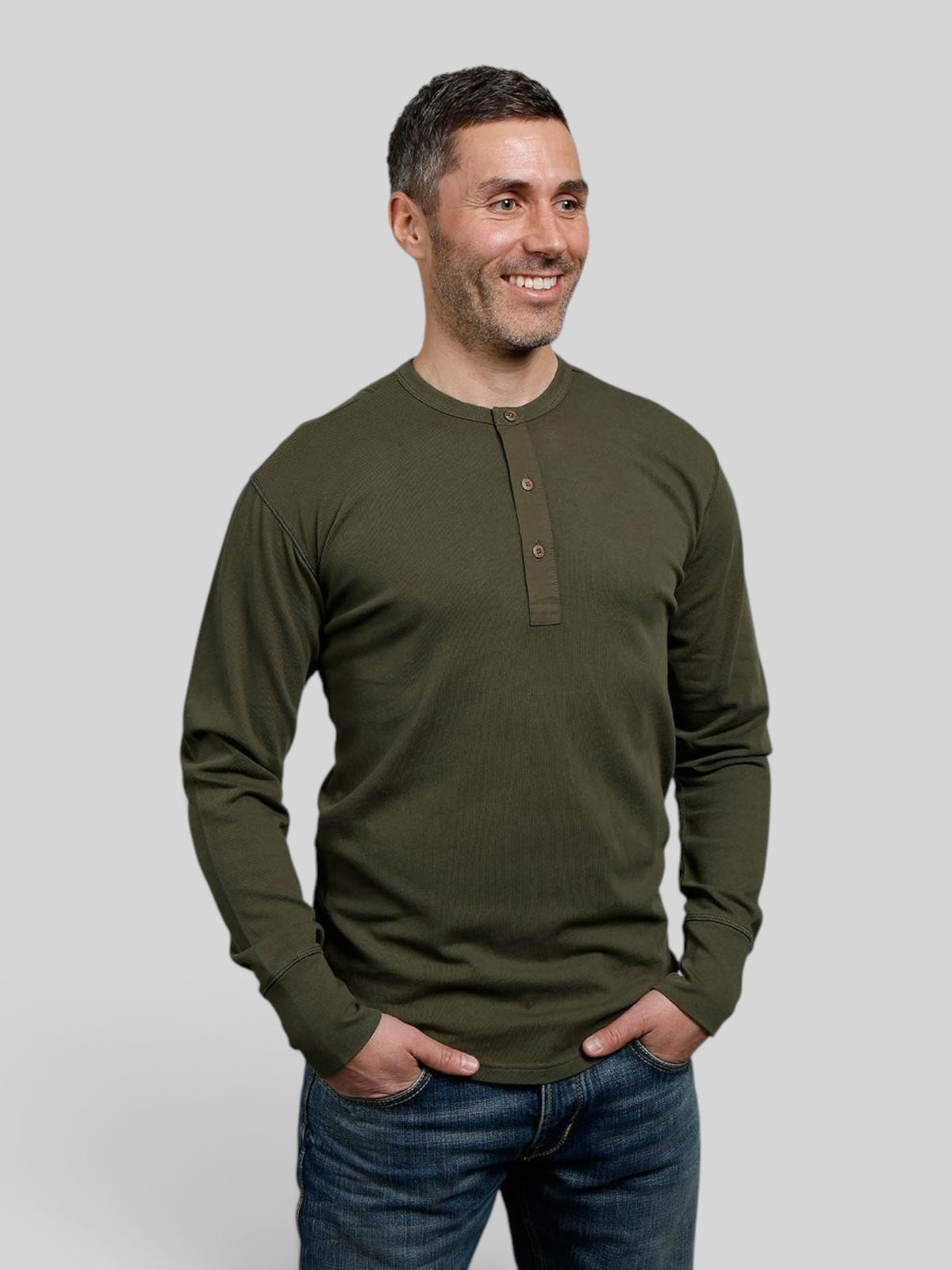 Baffle Haus 1927 Henley long sleeve shirt in Mojave green cotton with coconut buttons worn by a smiling man