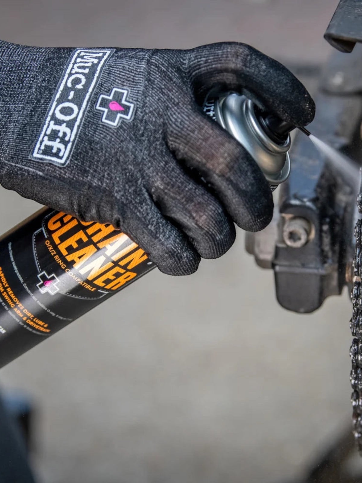 Baffle Haus motorcycle chain cleaner spray being applied to a dirty bike chain by a gloved hand